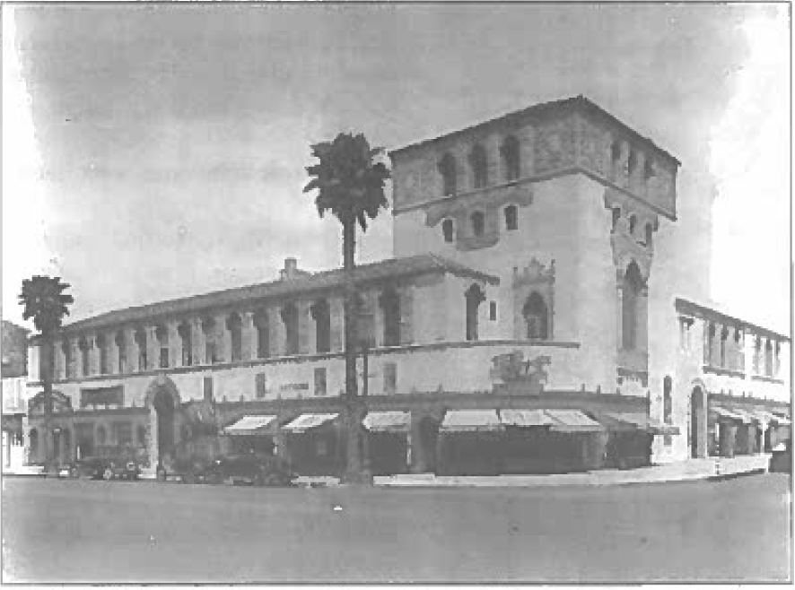 A Spanish colonial building with a corner tower. Palm trees line its side.